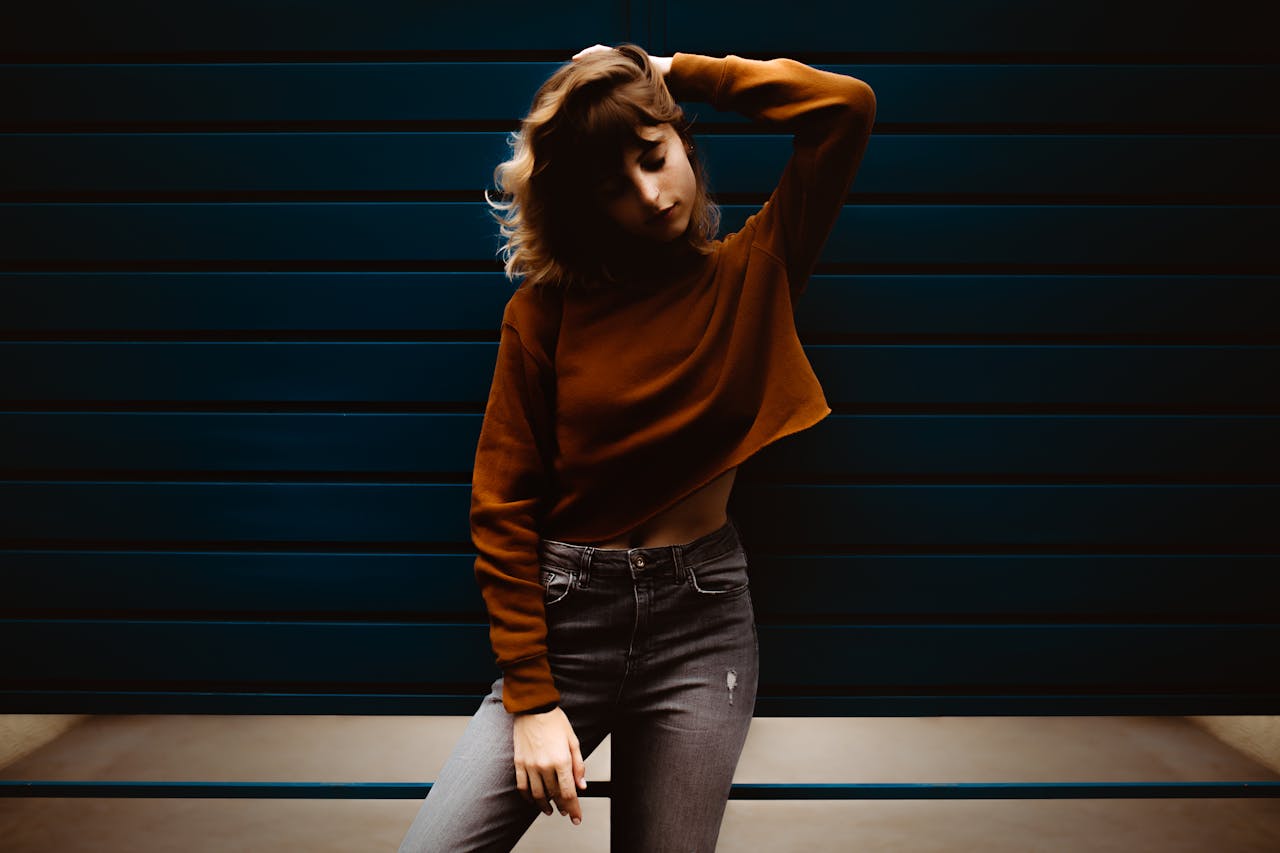 Stylish woman poses with hand in hair against a dark indoor backdrop. Artistic fashion photography.