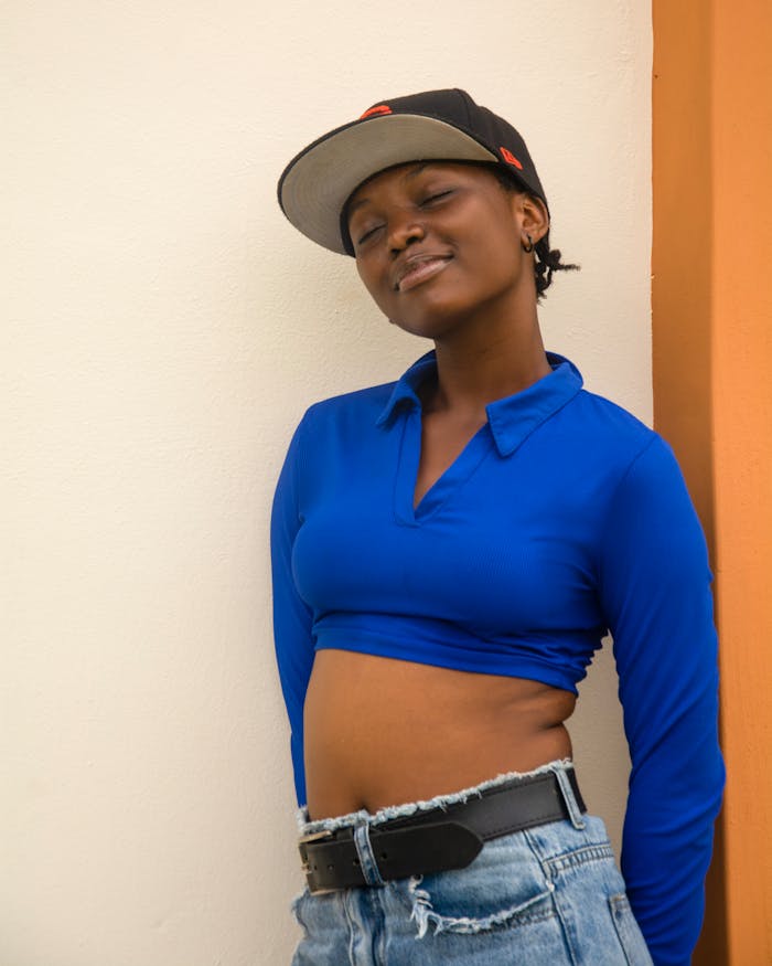 Smiling young woman in streetwear leaning against a wall, exuding confidence and style in an urban setting.