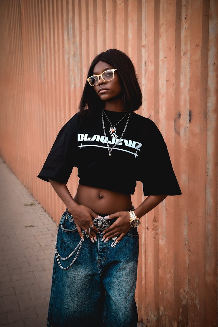 Trendy young woman in stylish streetwear posing against wall outdoors.